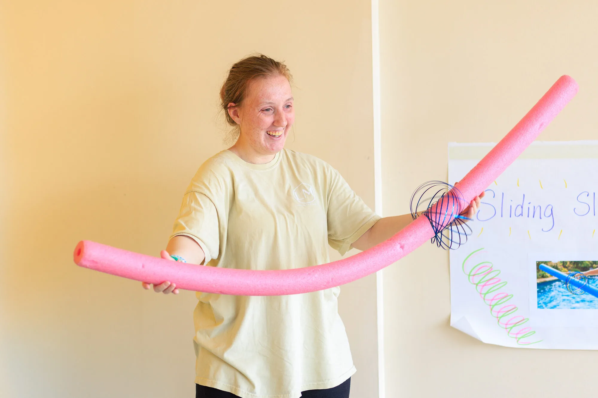 An educator holding a pool noodle beside a hand-lettered flip chart during a training activity